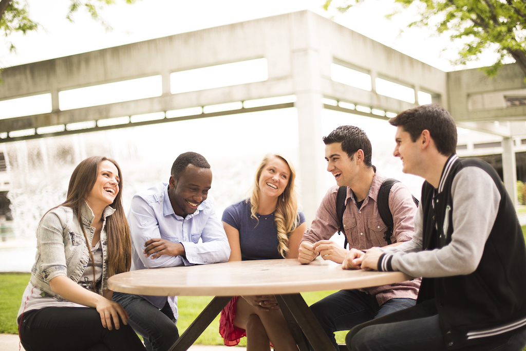 Five college students sit outside on a table laughing