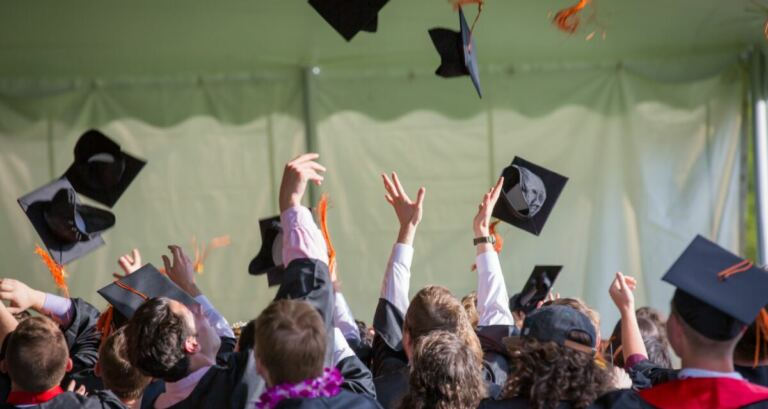 A crowd of college graduates throw their caps into the air