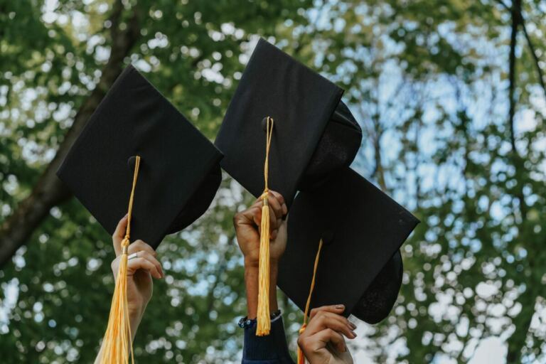 Three hands hold up graduation caps