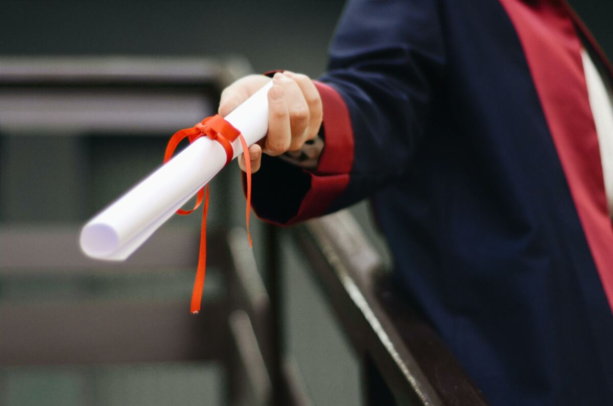 A graduate holds out their diploma