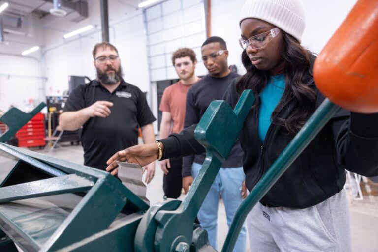 Student operates machinery while an instructor and other students observe