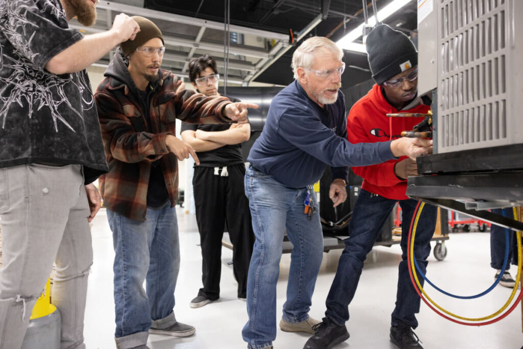 Instructor teaching HVAC maintenance in an air conditioning technology program practice lab on a college campus.