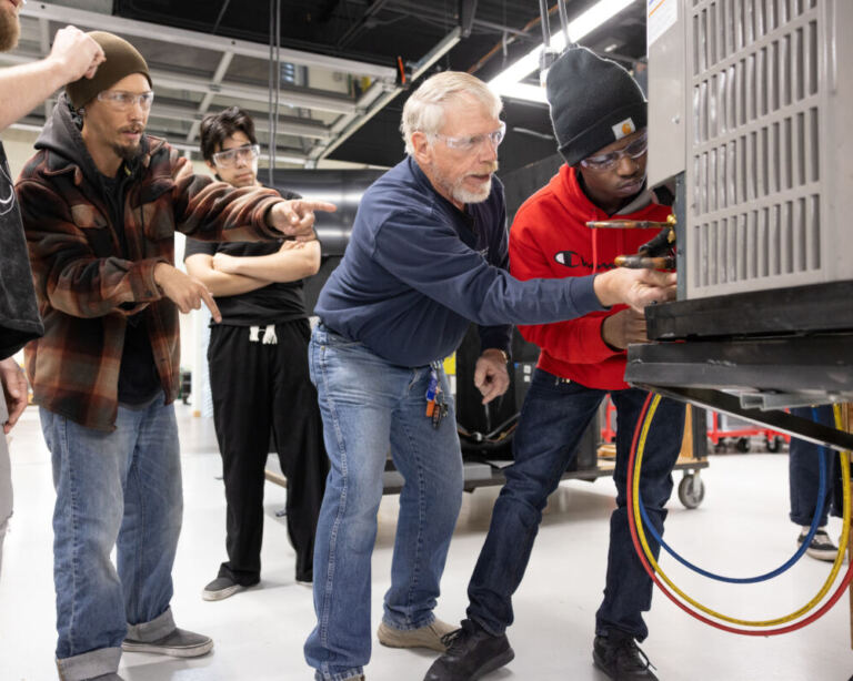 Instructor teaching HVAC maintenance in an air conditioning technology program practice lab on a college campus.