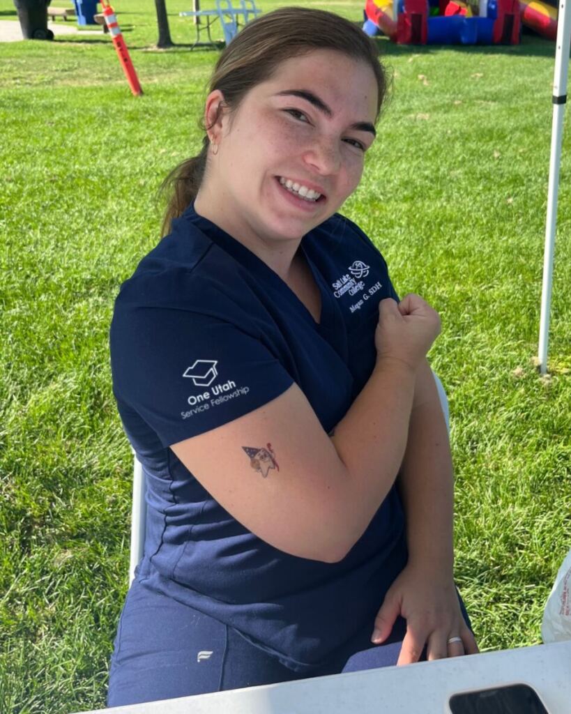 SLCC student wearing a One Utah Service Fellowship shows off a temporary cartoon tooth tattoo on her arm at a community resource fair.