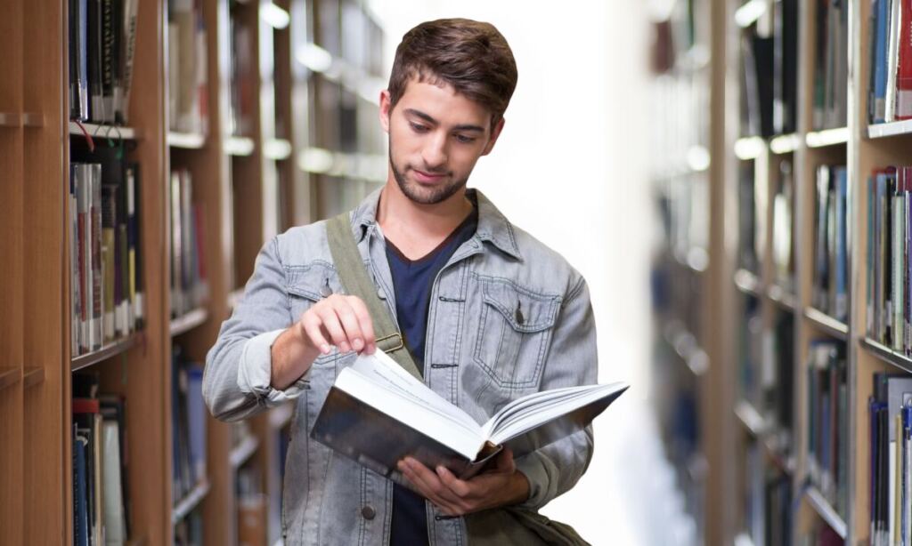 Student reading a book in the library between shelves